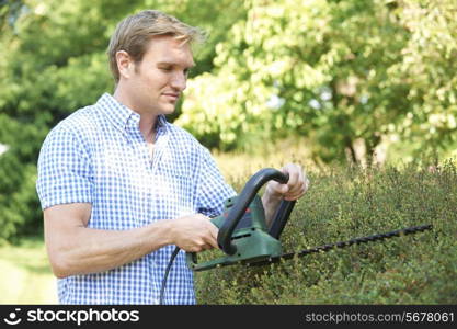 Man Cutting Garden Hedge With Electric Trimmer