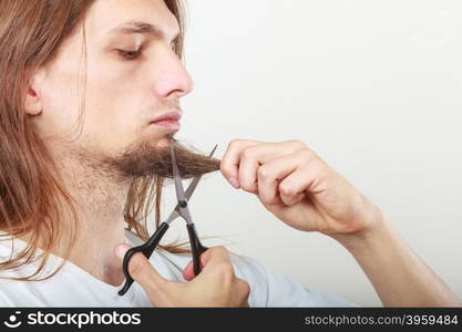 Man cutting his beard. Cut and shave concept. Young man with long beard holding scissors. Boy cutting hair on chin.