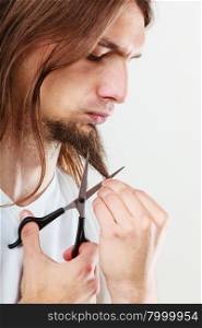Man cutting his beard. Cut and shave concept. Young man with long beard holding scissors. Boy cutting hair on chin.