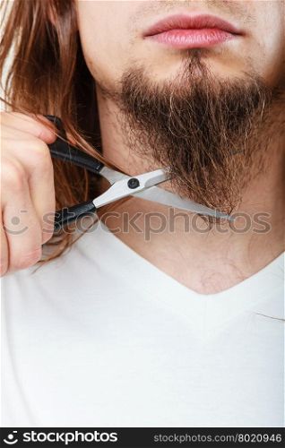 Man cutting his beard. Cut and shave concept. Young man with long beard holding scissors. Part face boy cutting hair on chin.
