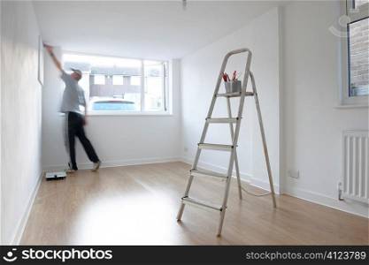 man decorating a room with ladder and paint pot in foreground