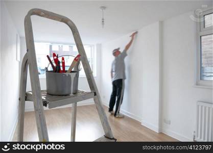 man decorating a room with ladder and paint pot in foreground