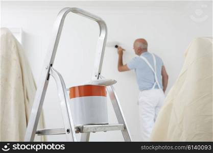 Man Decorating Room With Can Of Paint And Brush In Foreground