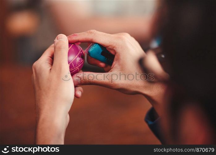Man decorating the Easter eggs by scratching patterns on dyed eggs. Traditional Easter time, spring time, new beginnings. Candid people, real moments, authentic situations