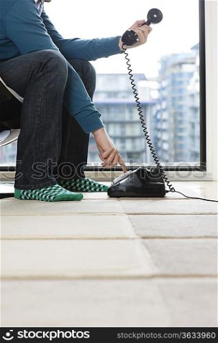 Man dialing phone at home, low section, side view
