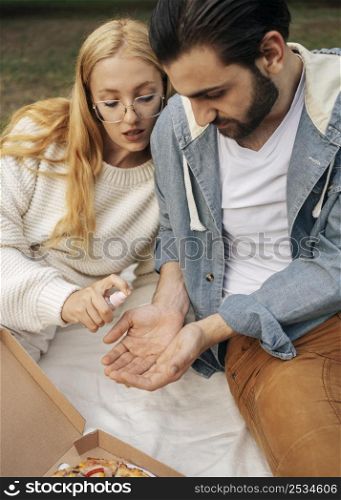 man disinfecting his girlfriend s hands before having picnic