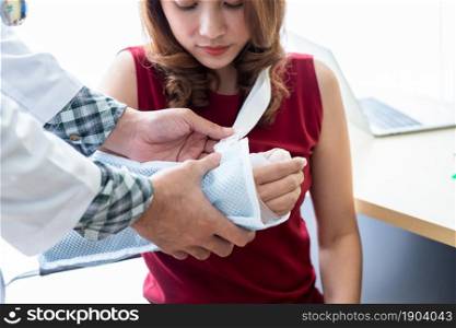 man doctor with wrapping nurse bandages splint to the arm of a female patient wear arm splint with analogue pressure gauge for better healing In the room hospital background.