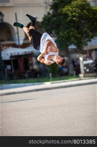 Man doing acrobatic tricks in city street. Young sportsman performing his acrobatic skills in doing somersault. Show in the city street