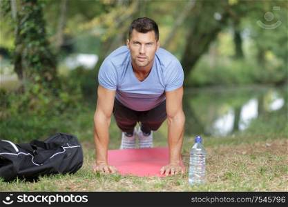 man doing plank exercise on grass in summer park