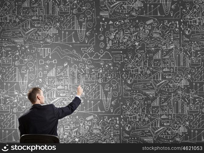 Man draw on chalkboard. Rear view of businessman drawing with chalk business sketches on wall