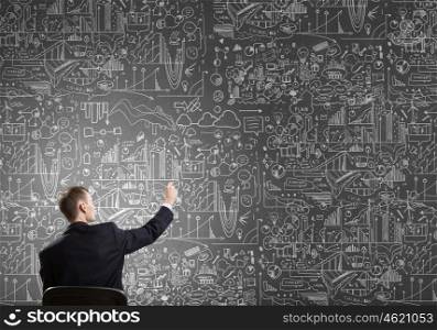 Man draw on chalkboard. Rear view of businessman drawing with chalk business sketches on wall
