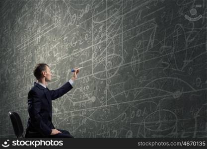 Man draw on chalkboard. Rear view of businessman drawing with marker business sketches on wall