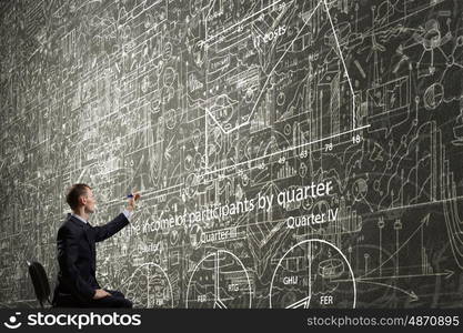 Man draw on chalkboard. Rear view of businessman drawing with marker business sketches on wall