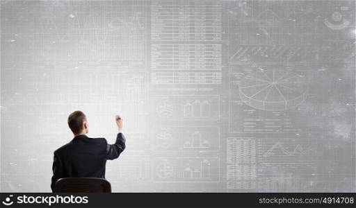 Man draw on chalkboard. Rear view of businessman drawing with marker business sketches on wall