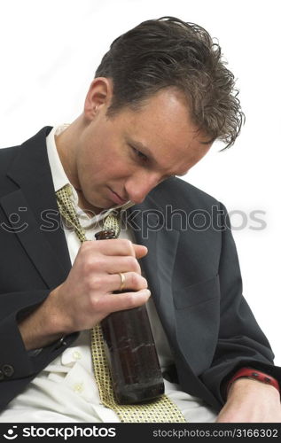 Man dressed in business attire sitting drunk with a beer bottle in his hand looking depressed