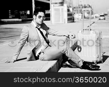 Man dressed in suit and suitcase sitting on the floor in the street