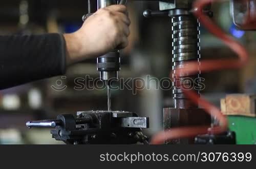 Man drilling in steel plate with bench drill. Close up vertical drilling machine with manual pressure, worker placing lubricating oil on a drill during metal work.