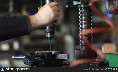 Man drilling in steel plate with bench drill. Close up vertical drilling machine with manual pressure, worker placing lubricating oil on a drill during metal work.