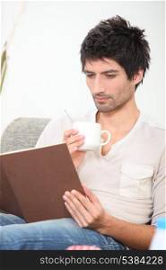 Man drinking a hot drink and reading a book