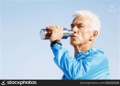 Man drinking from a sports bottle. Handsome healthy man in sport wear drinking from sports bottle