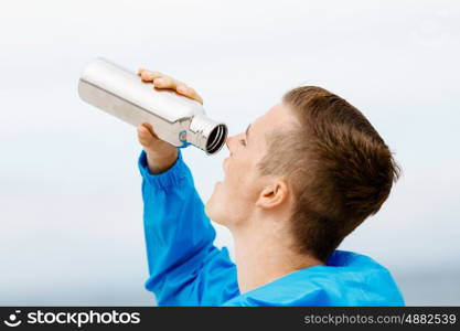 Man drinking from a sports bottle. Young man in sport wear drinking from sports bottle