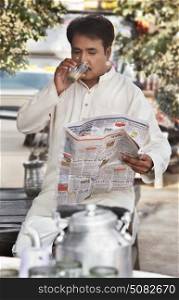 Man drinking tea and reading a newspaper at tea stall