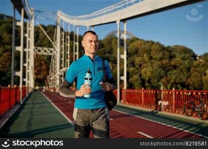 Man drinking water after running workout in morning. Portrait of fitness sportsman runner after doing cardio training outdoors having relax and rest. Man drinking water after running workout in morning