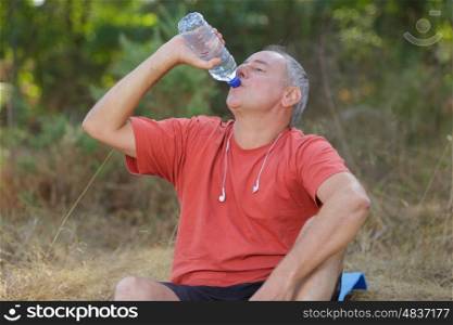 man drinking water bottle in a park