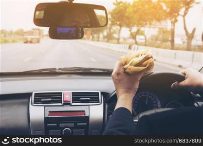 Man driving car while eating hamburger