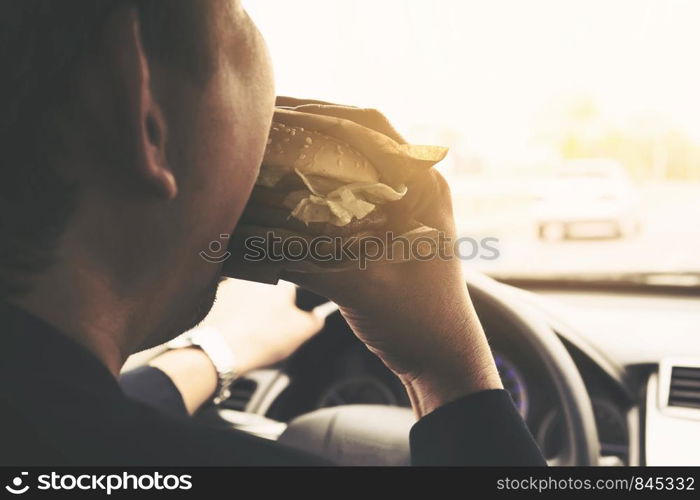 Man driving car while eating hamburger