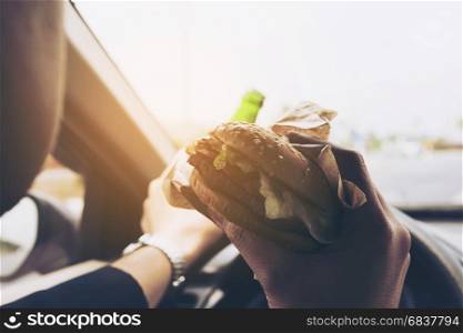 Man driving car while eating hamburger and drink beer