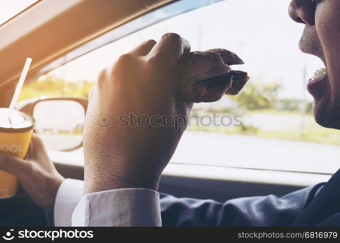 Man driving car while holding a cup of cold coffee and eating hamburger