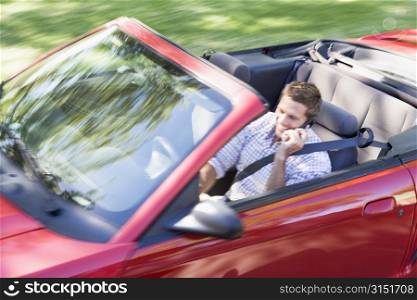 Man driving convertible car using cellular phone and smiling