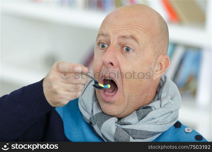 man eating a spoon full of medicine tablets and pills