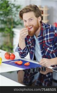 man eating a tomato while preparing them at home