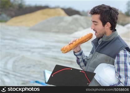 Man eating baguette on building site