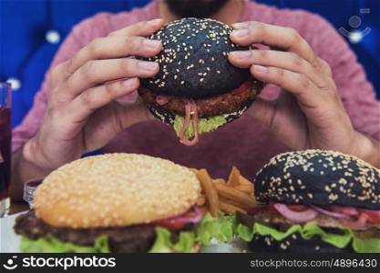 Man eating burgers at table, closeup photo