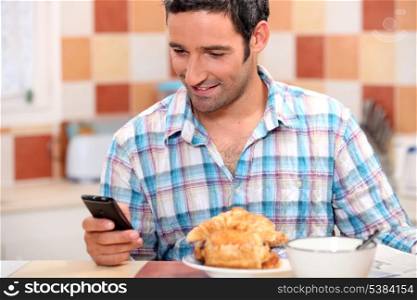 Man eating croissant and texting