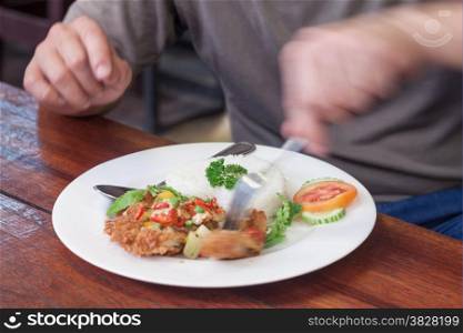Man eating fried chicken wing and jasmine rice on white plate-meal time
