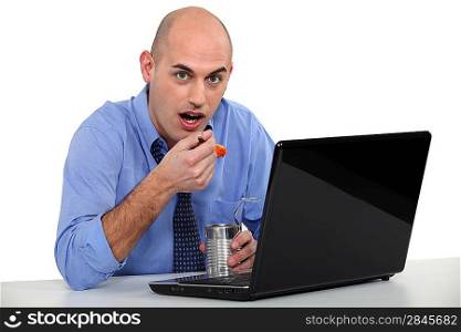 Man eating tinned food in front of his laptop
