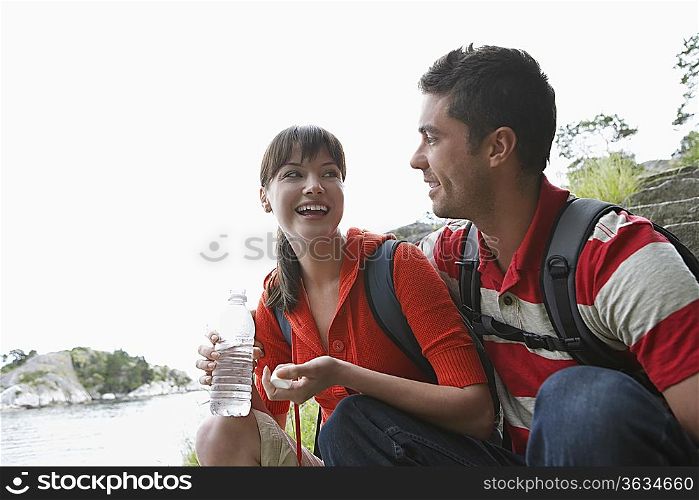 Man embracing woman holding water bottle, near ocean