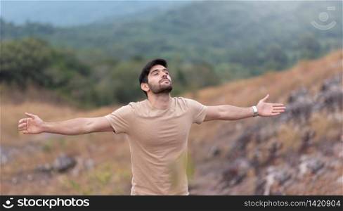 Man enjoying feeling carefree freedom with open arms over nature background in the morning. Bearded man eyes closed standing breathing fresh air on top of mountain.