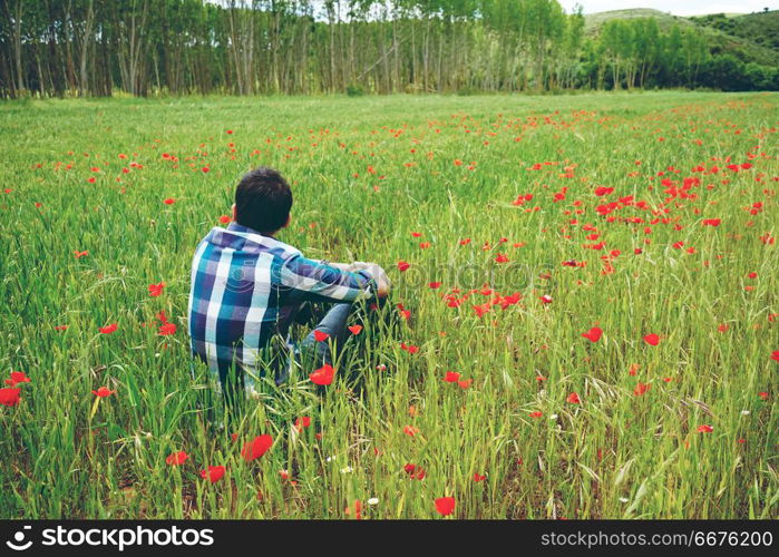 Man enjoying the day in a field of green wheat and flowers