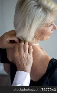 Man fastening his wife&rsquo;s pearl necklace