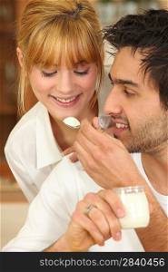 Man feeding a spoonful of yoghurt to his girlfriend