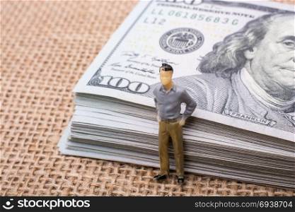 Man figurine standing beside the bundle of US dollar