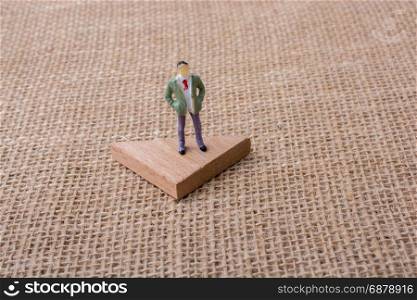 Man figurine standing on a triangle piece of wood