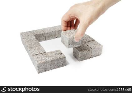 Man finishing a square made of small blocks of granite rock.