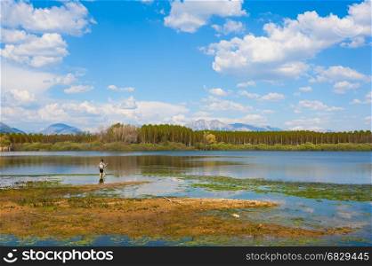 Man fishing from the shore of lake . Landscape with lake,forest,blue sky and cloud.