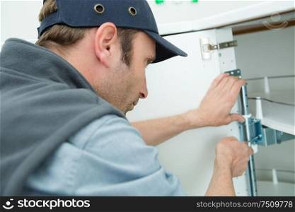 man fitting hinge to kitchen corner cupboard base unit